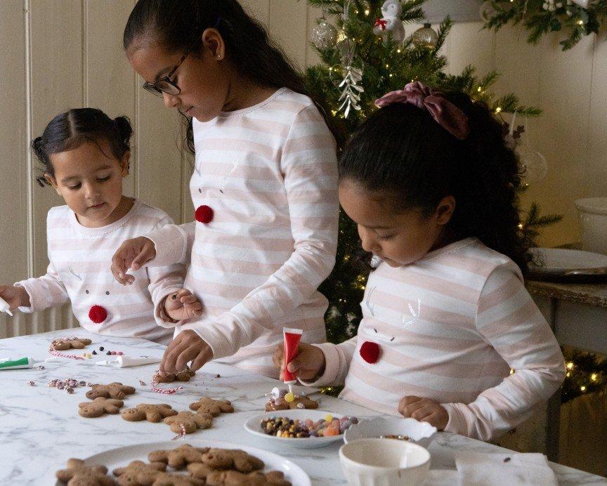 three girls are making cookies at a table with a christmas tree