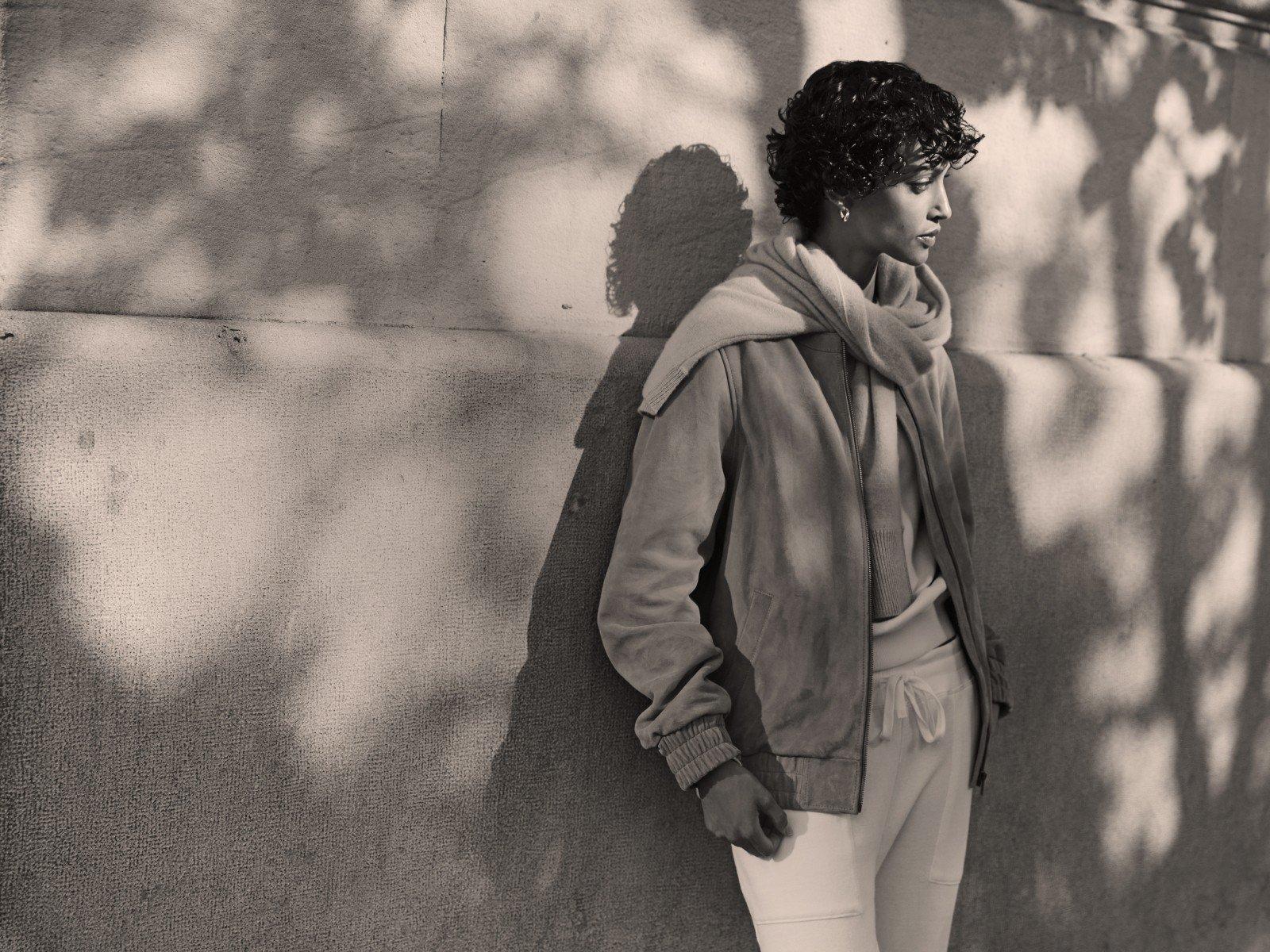 a woman leaning against a wall with her hands in her pockets