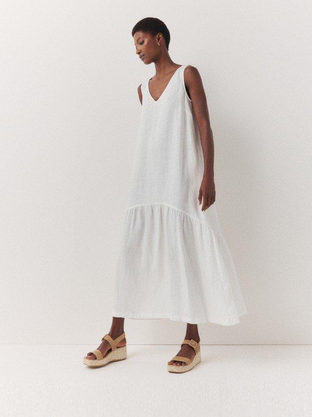 the model is wearing a white linen dress and sandals