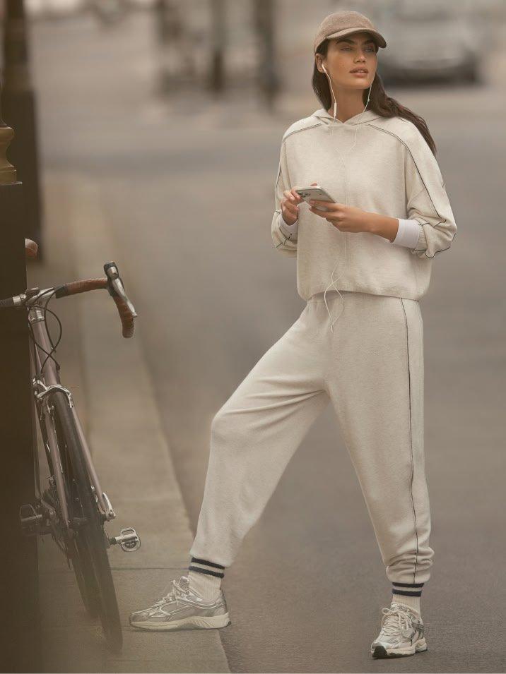 a woman in white outfit leaning against a bike while looking at her phone