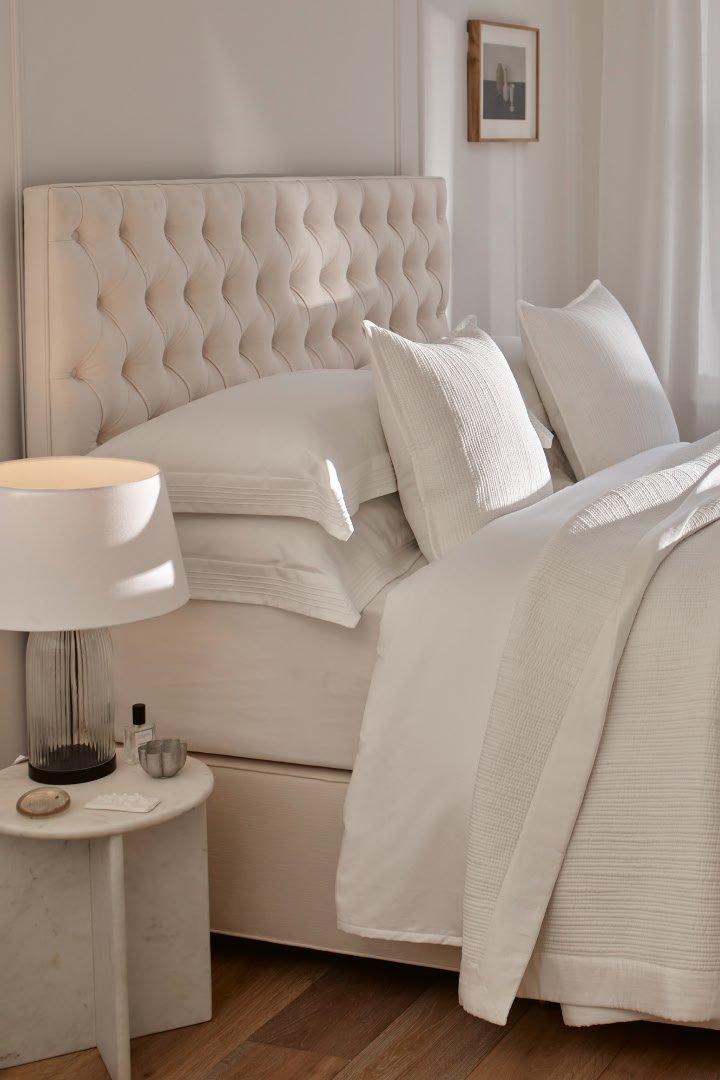 a white bed with white sheets and pillows in a bedroom