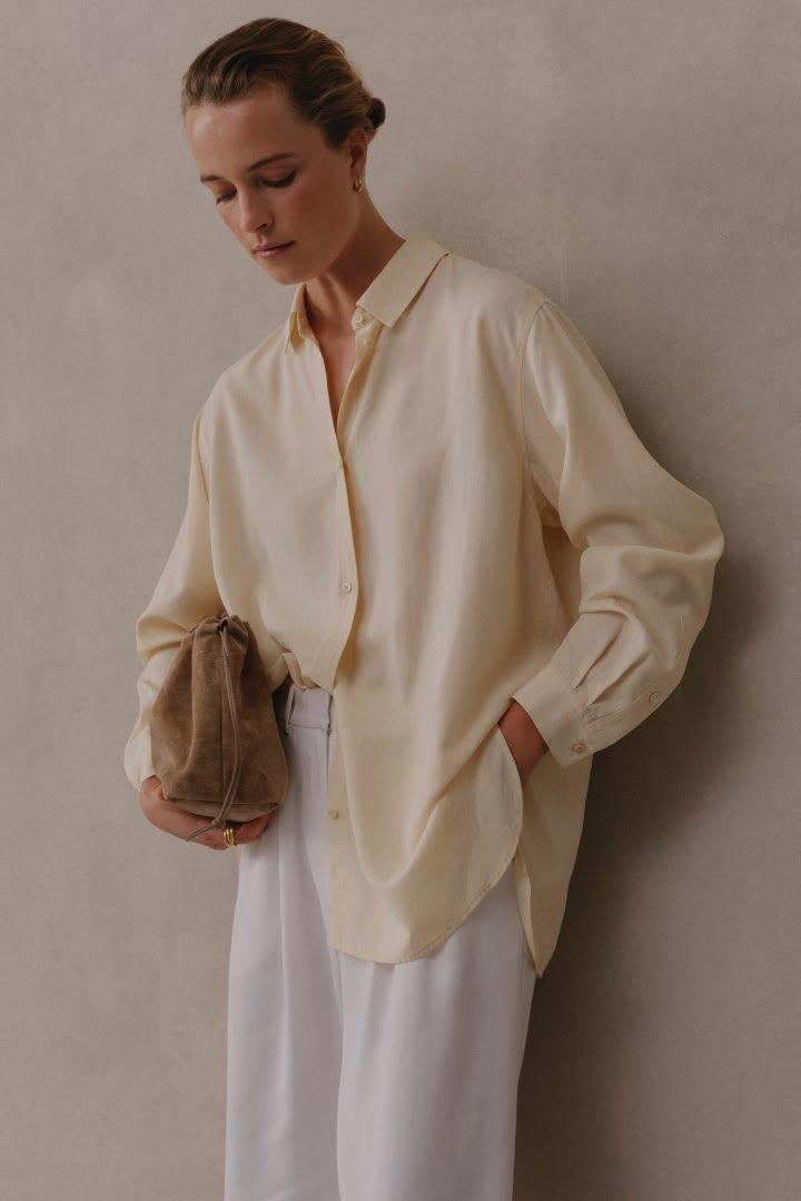 a woman in white pants and a cream shirt holding a brown bag