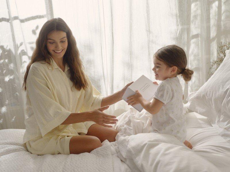 a woman and child sitting on a bed with a paper