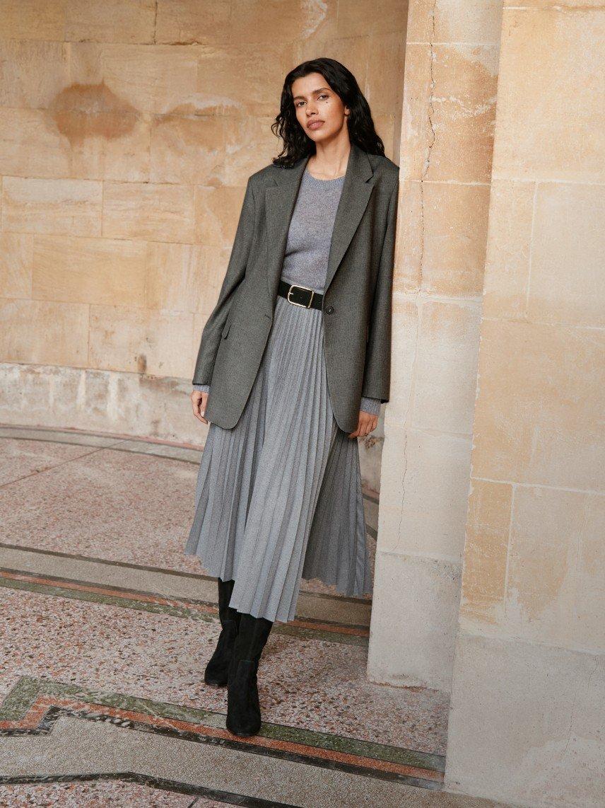 a woman in a grey dress and black boots standing in a corner