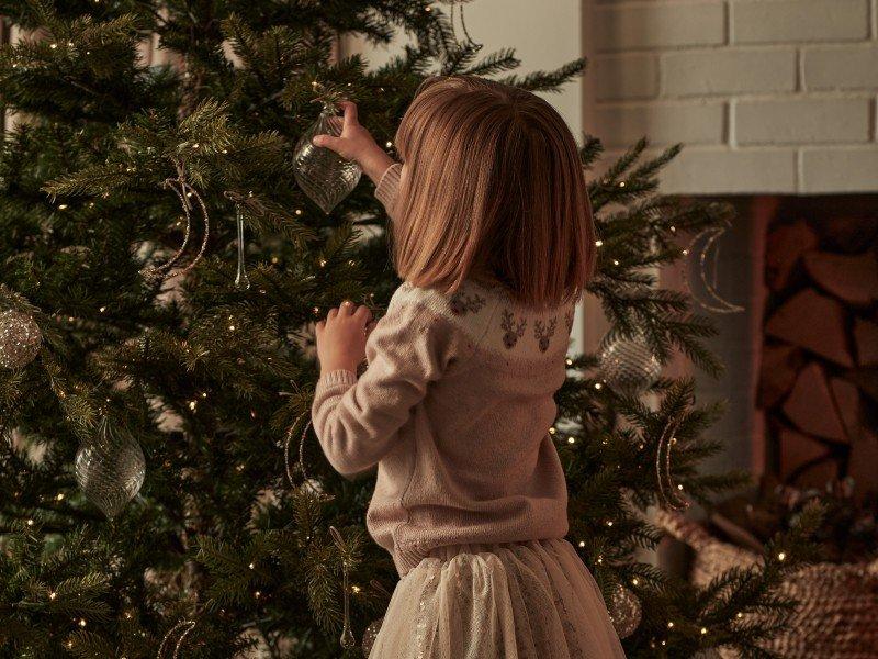 a little girl decorating a christmas tree in a living room