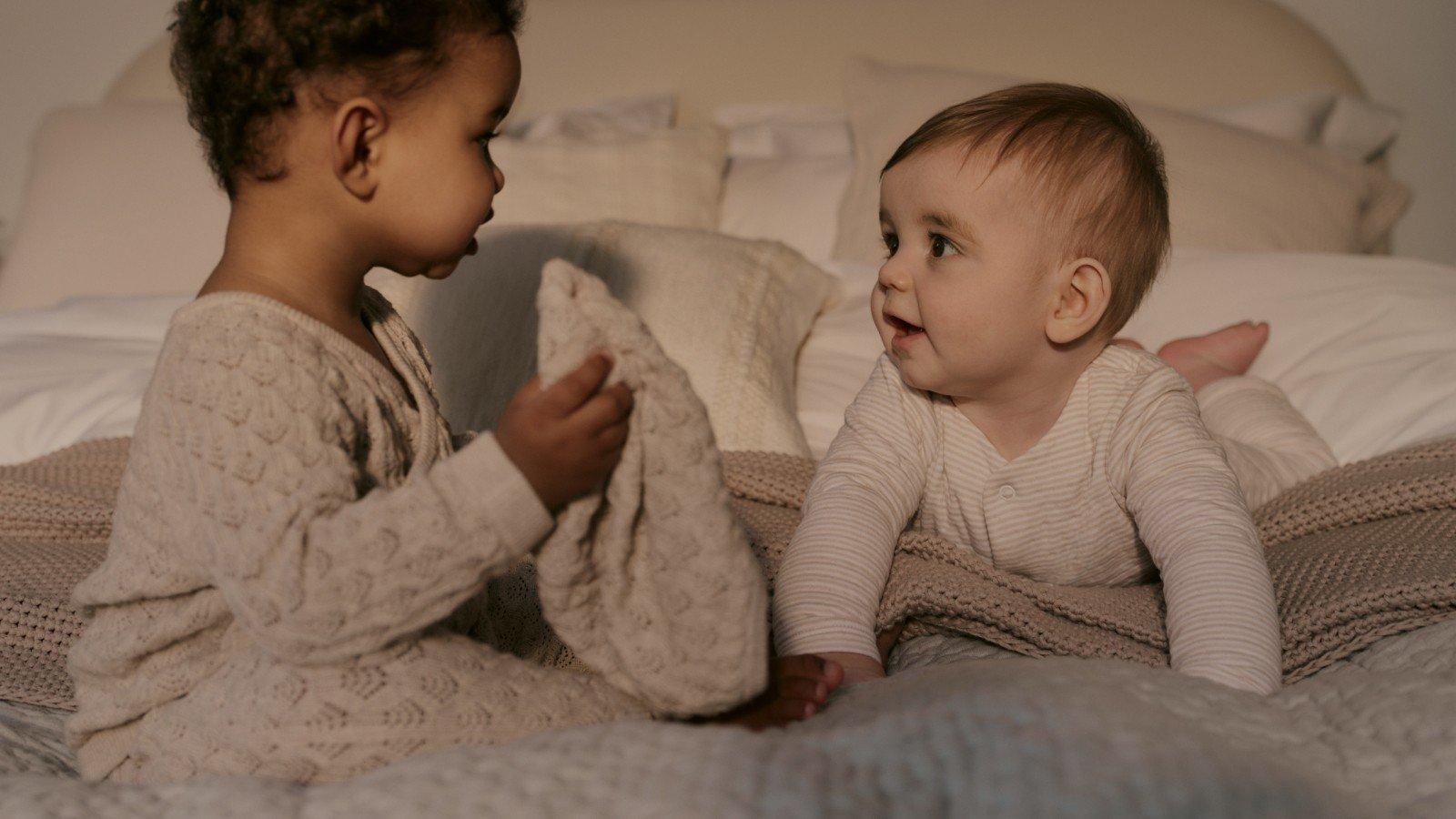 two babies playing on a bed with a blanket and a toy