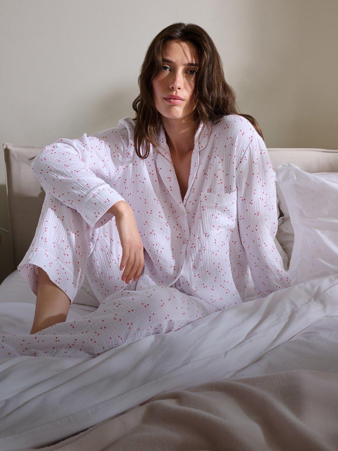 a woman sitting on a bed in a white pajama set