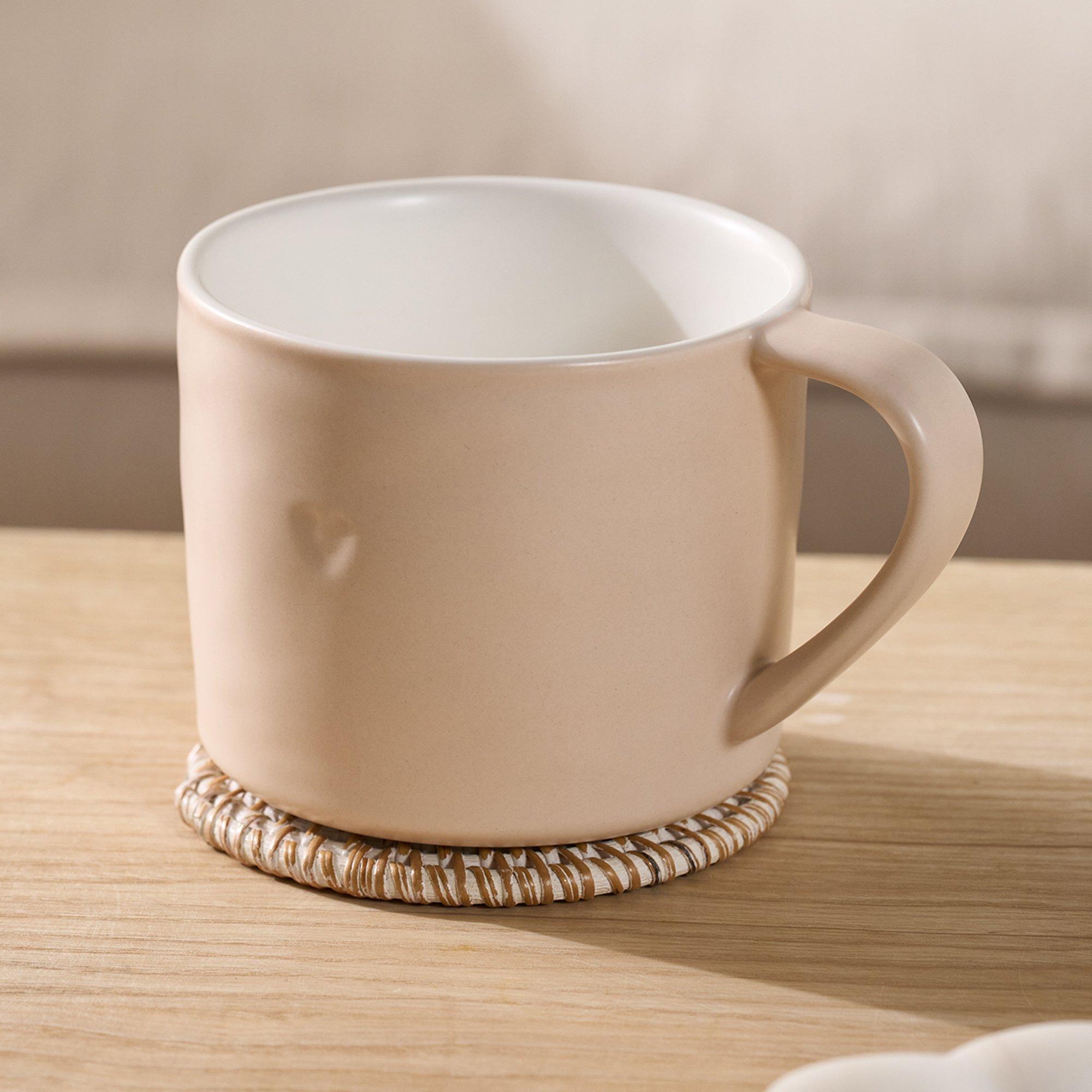 a coffee cup sitting on a wooden table with a white plate