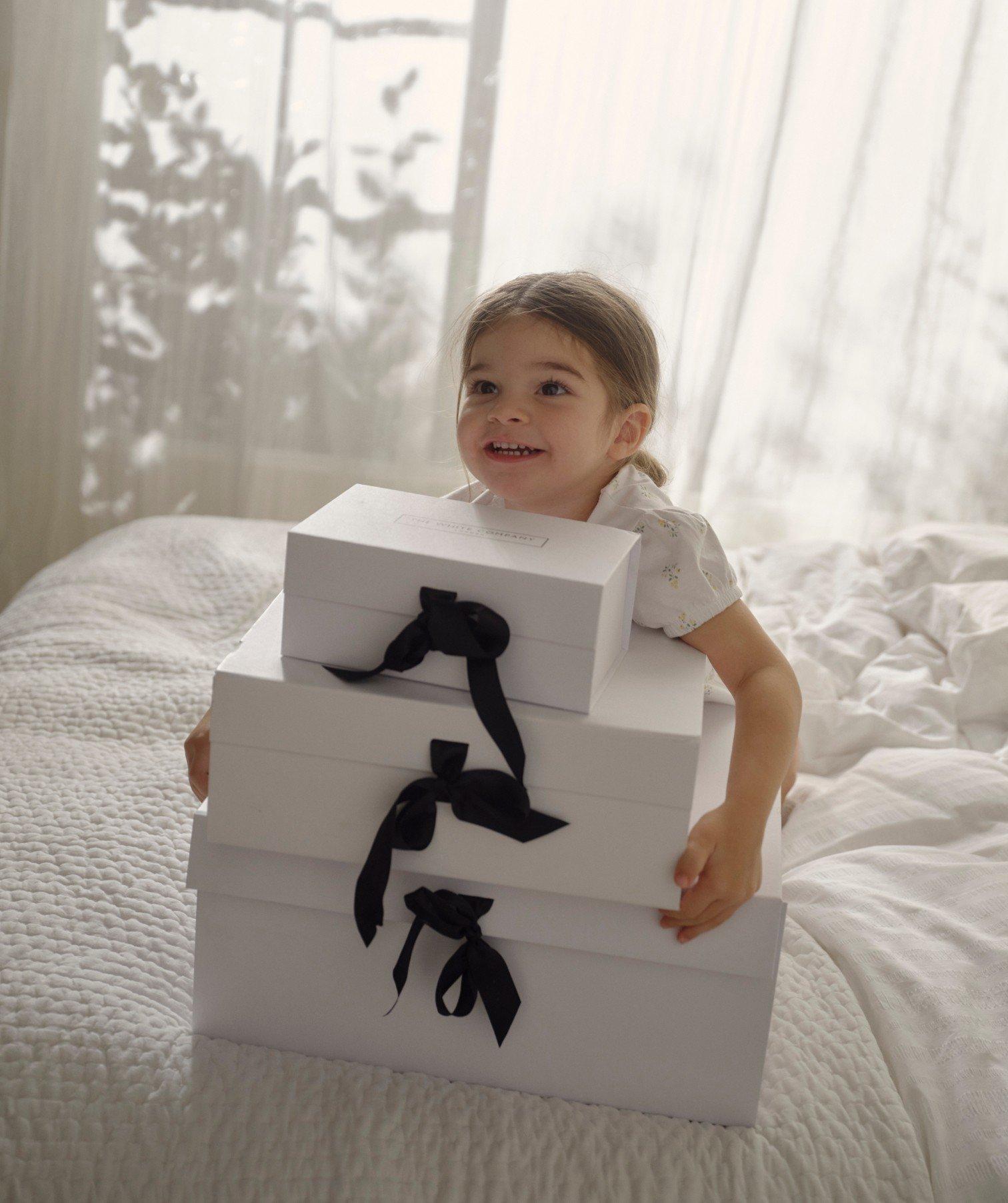 a little girl sitting on a bed with a bunch of boxes