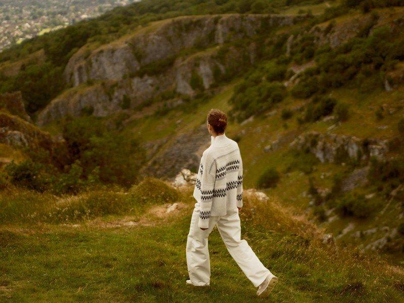 a person walking on a grassy hillside with a white jacket