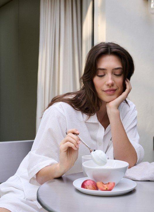 a woman in a grey sweater and white pants leaning against a wall