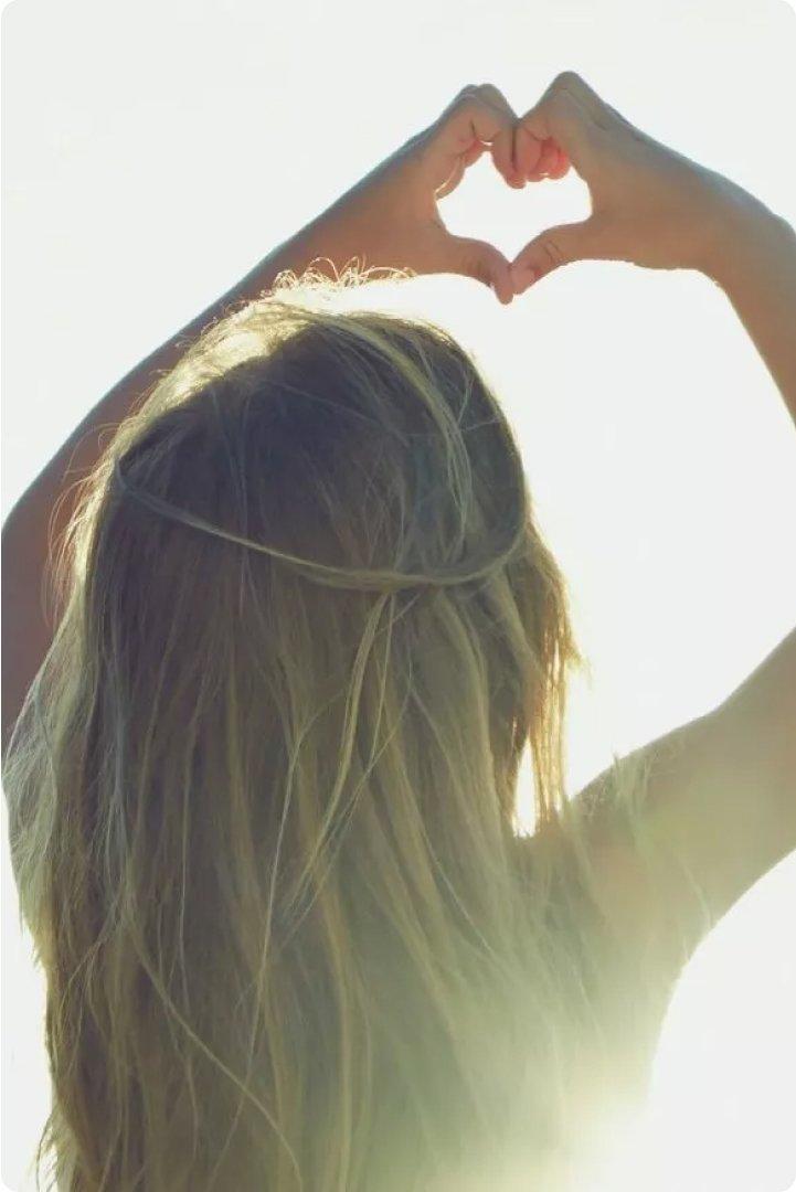 a girl making a heart shape with her hands in the sun