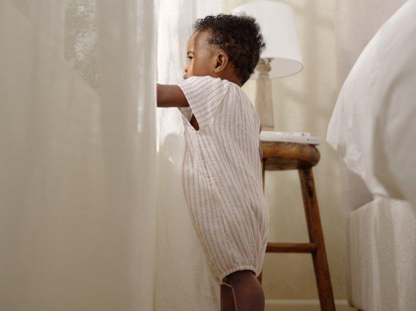 a baby standing on a bed looking out a window
