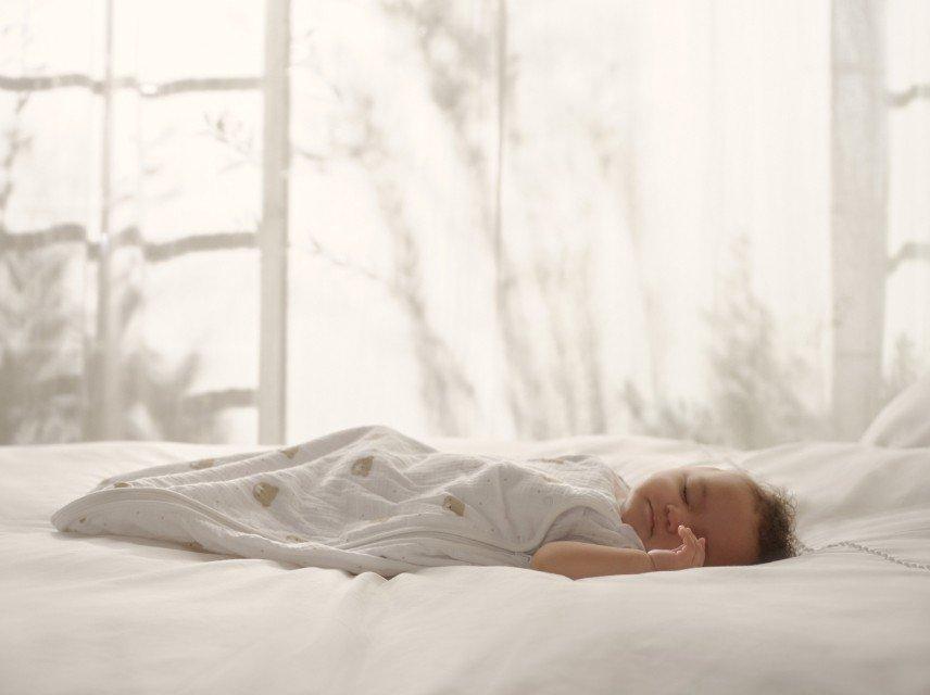 a baby sleeping on a bed with white sheets and curtains