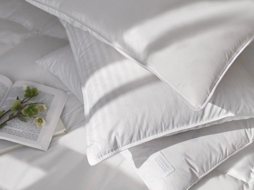 a pile of pillows on a bed with a book and flowers
