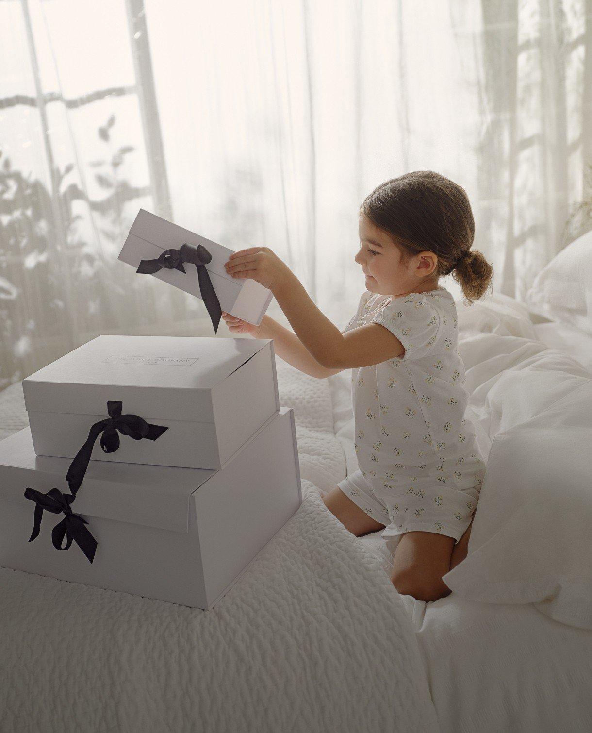 a little girl sitting on a bed opening a box