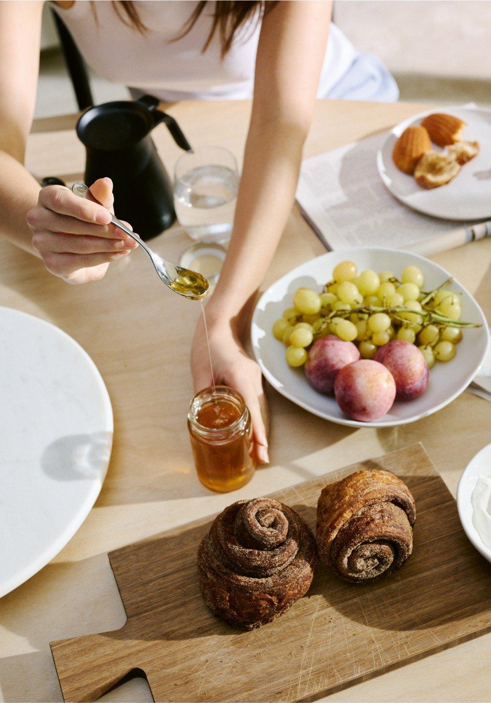 a woman is pouring honey on a plate of fruit and bread
