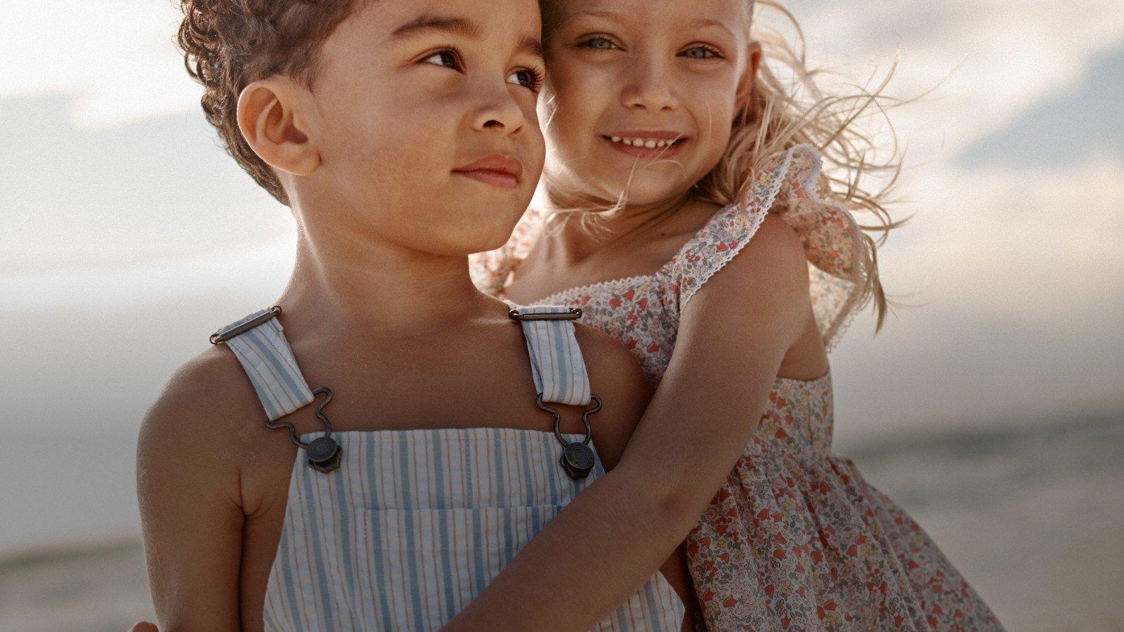 a young boy and girl hugging each other on a beach