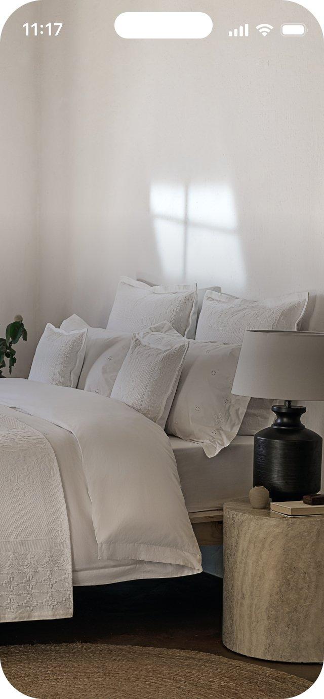 a white bed with pillows and a night stand next to a window