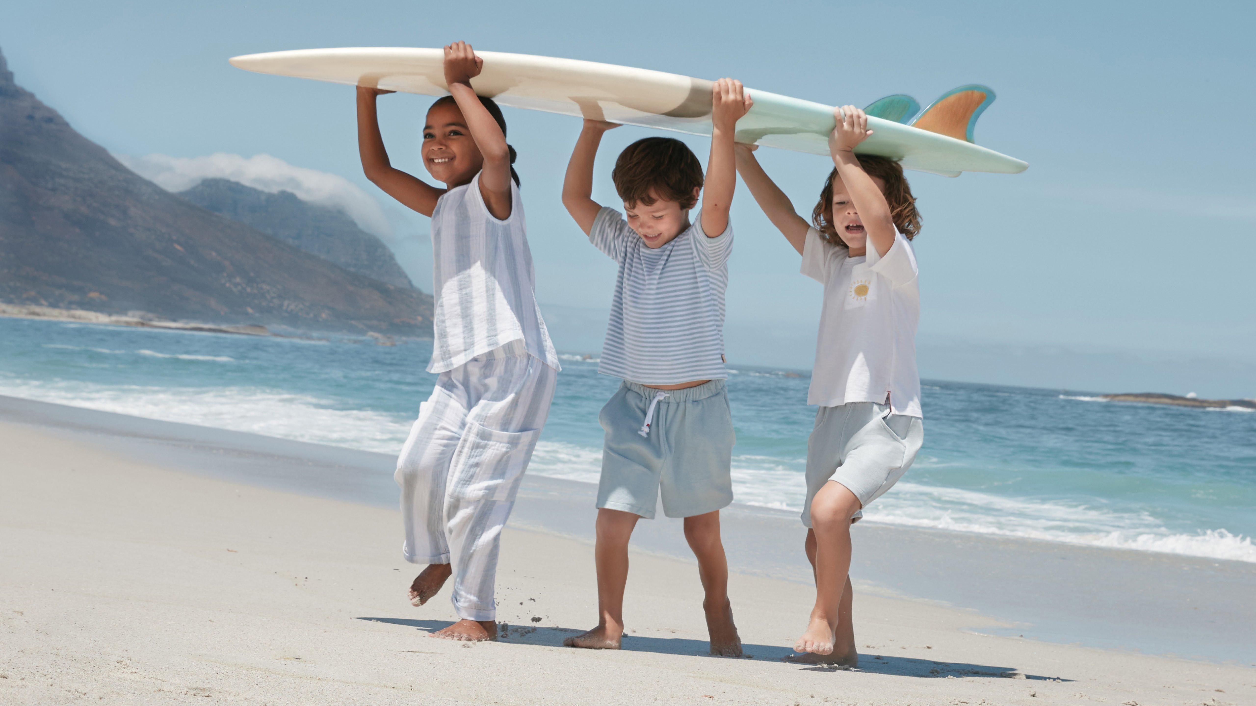 three children carrying a surfboard on the beach