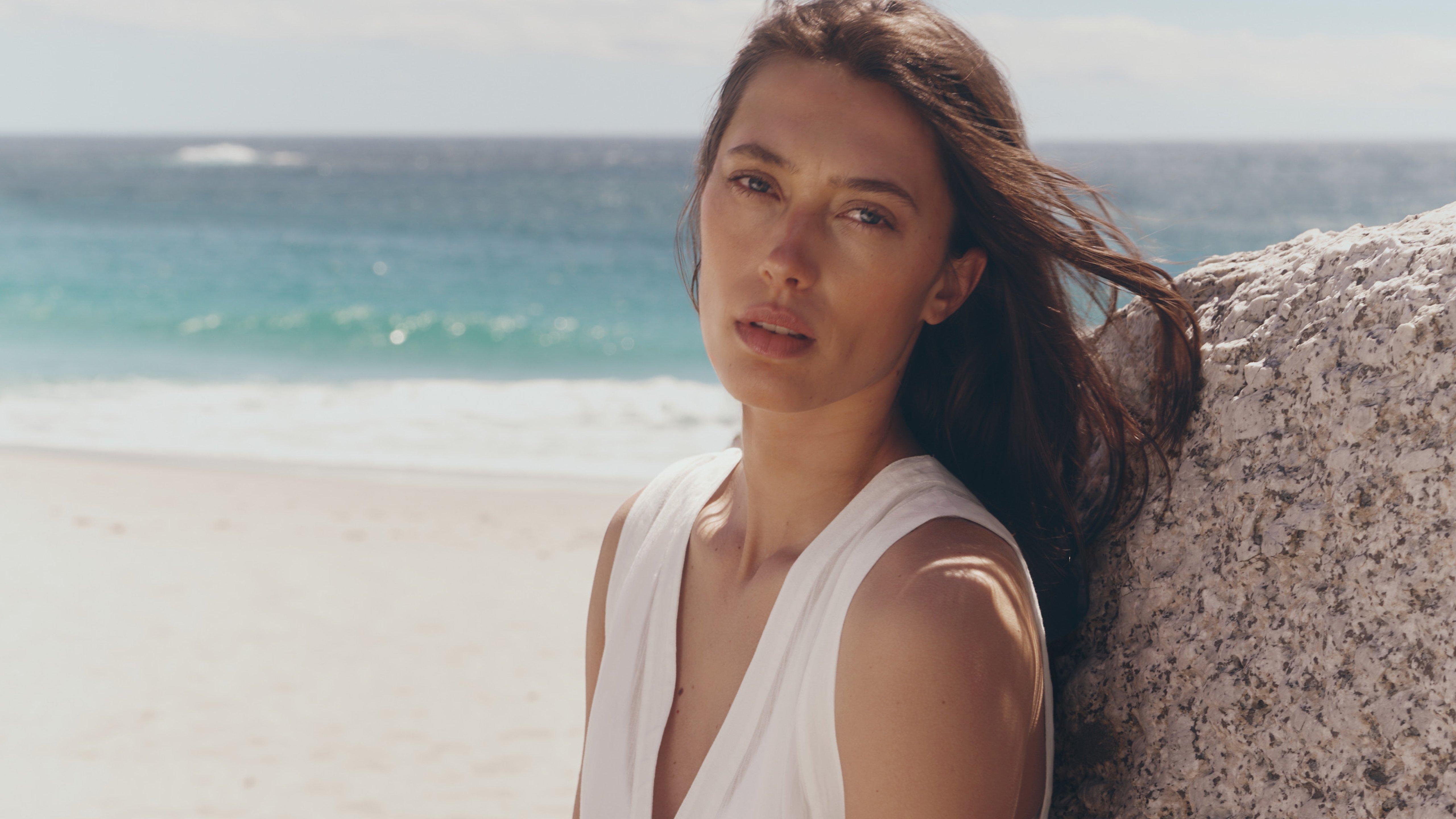a woman sitting on a rock at the beach with her hair blowing in the wind