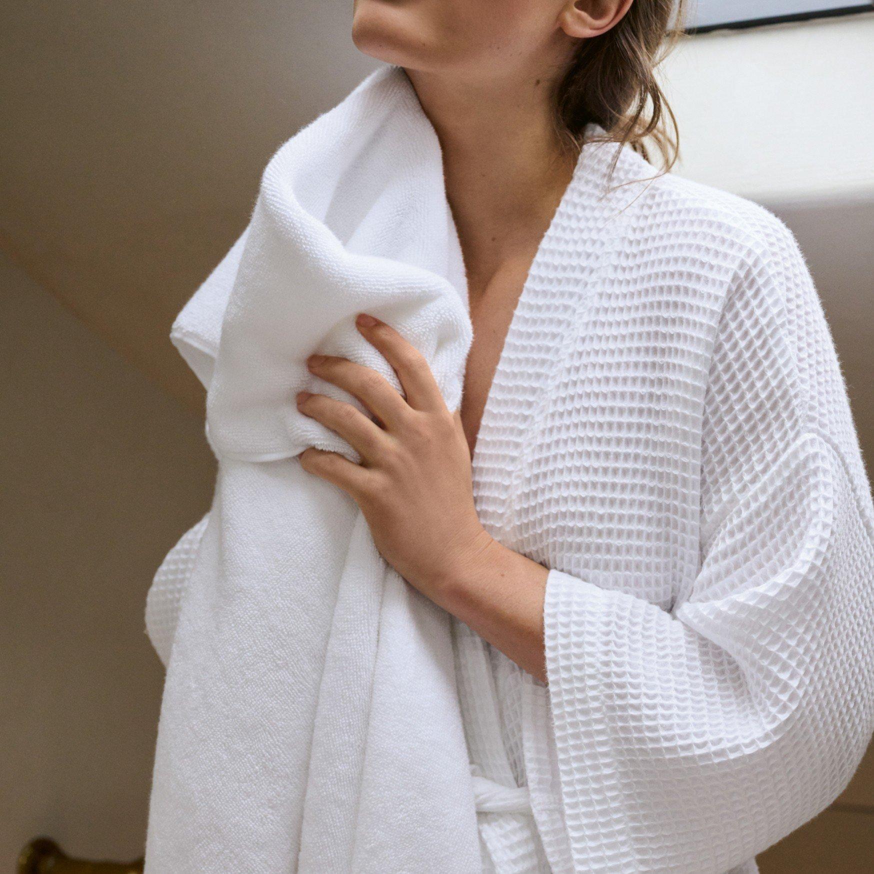 a woman in a white robe holding a towel to her face