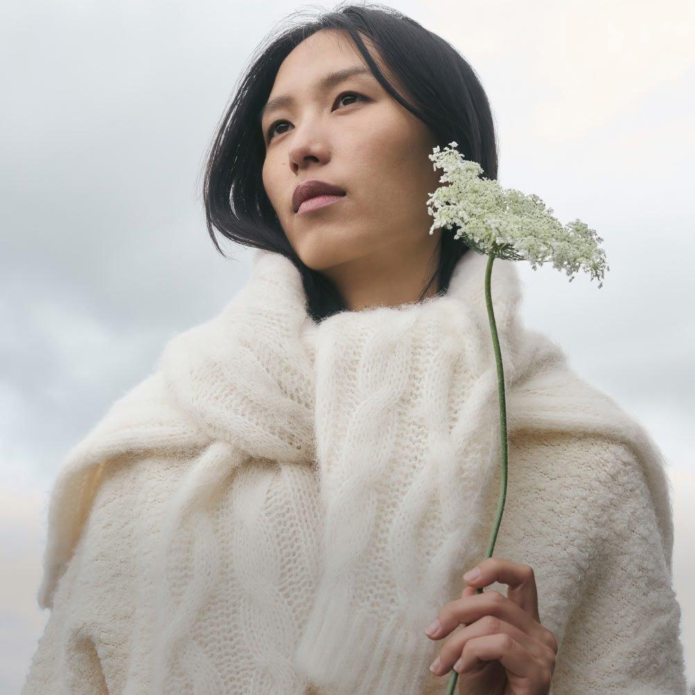 a woman in a white sweater holding a flower in her hand