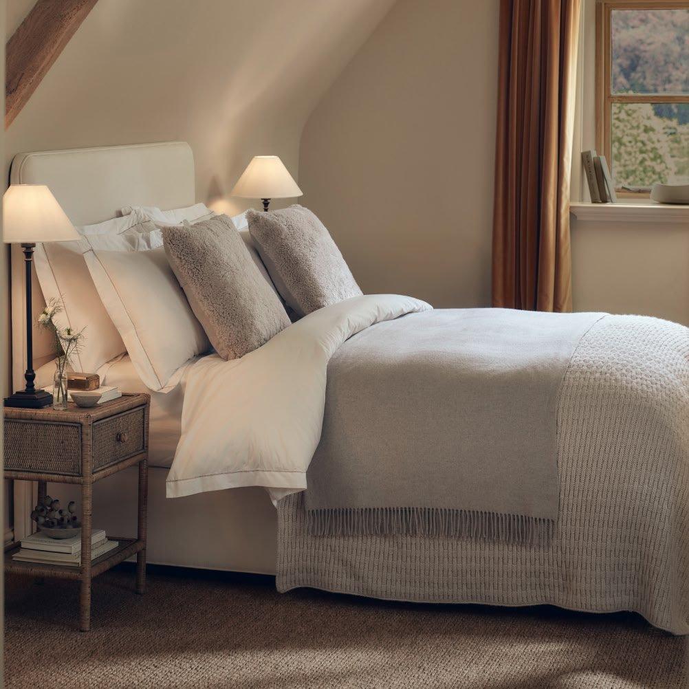 a bed with a white comforter and pillows in a room with a window