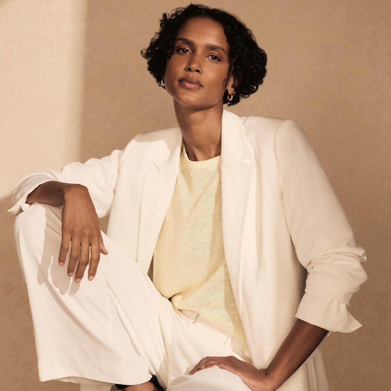 a woman in a white suit sitting on a stool