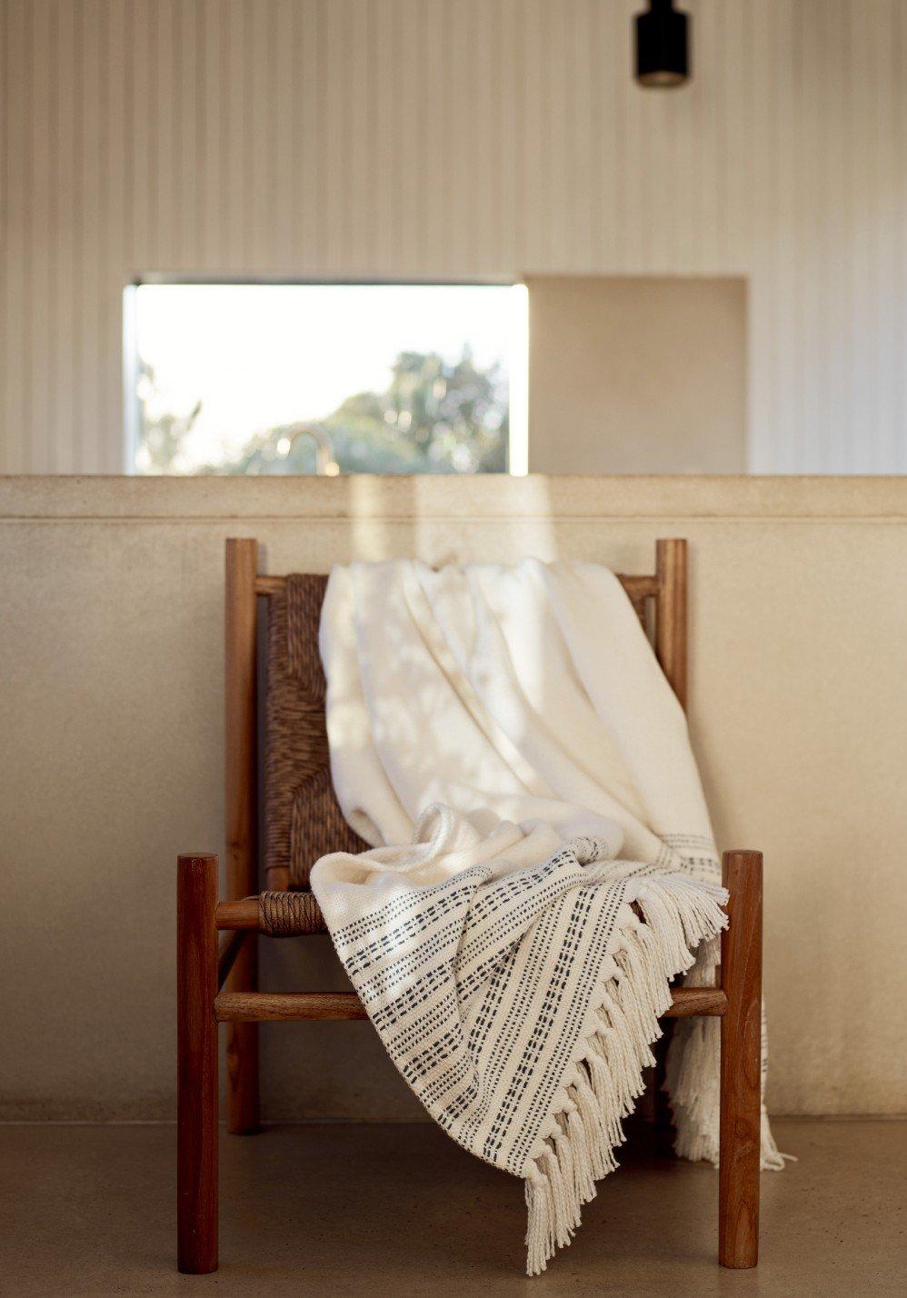 a woman in a grey sweater and white pants leaning against a wall