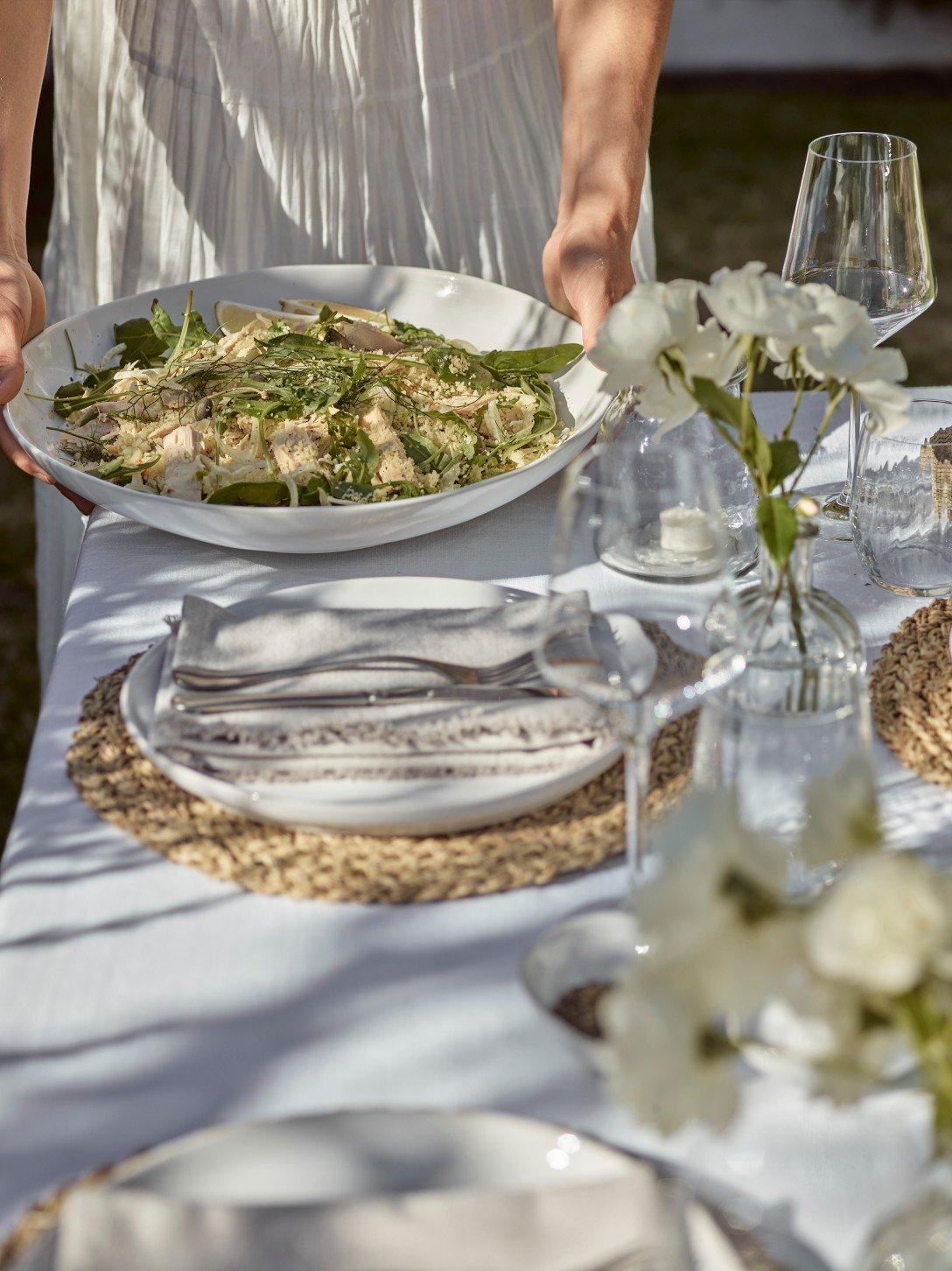 a woman holding a plate of food on a table with white table cloth