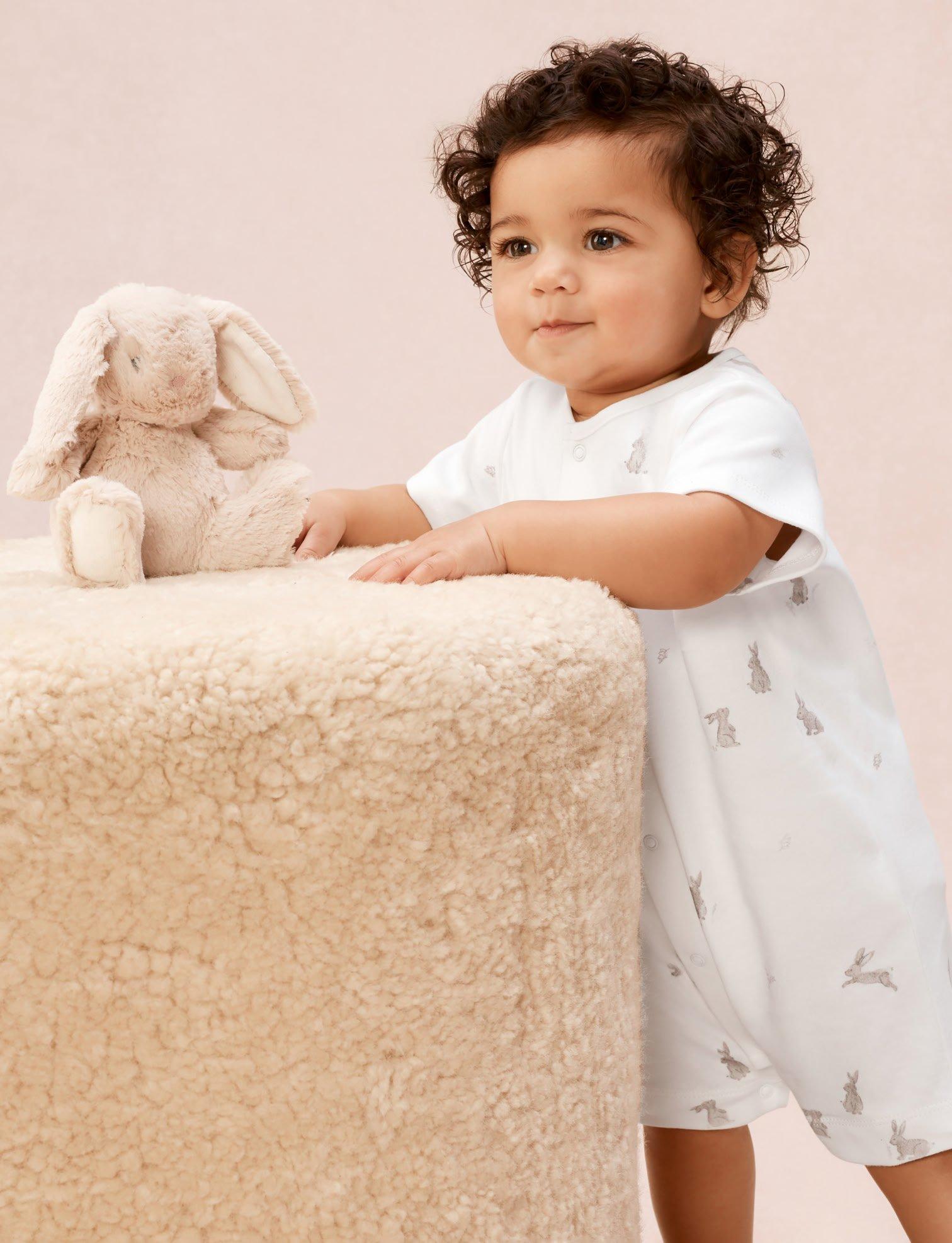 a baby in white pajamas standing next to a stuffed animal