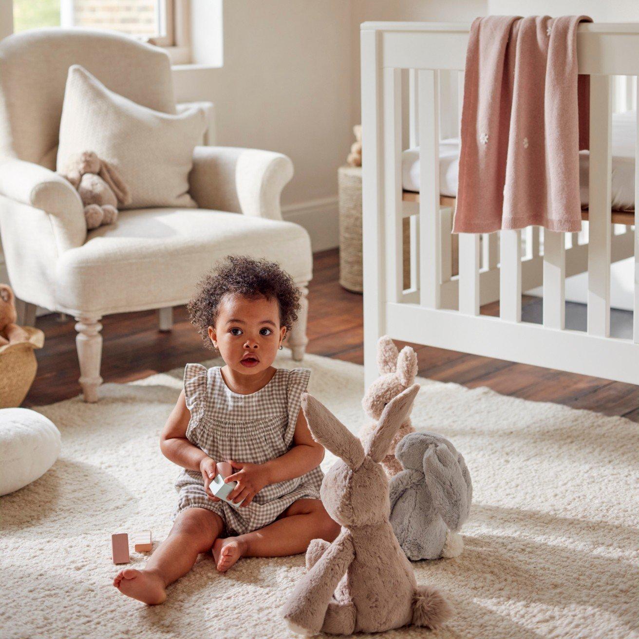 a baby sitting on a white rug in a nursery