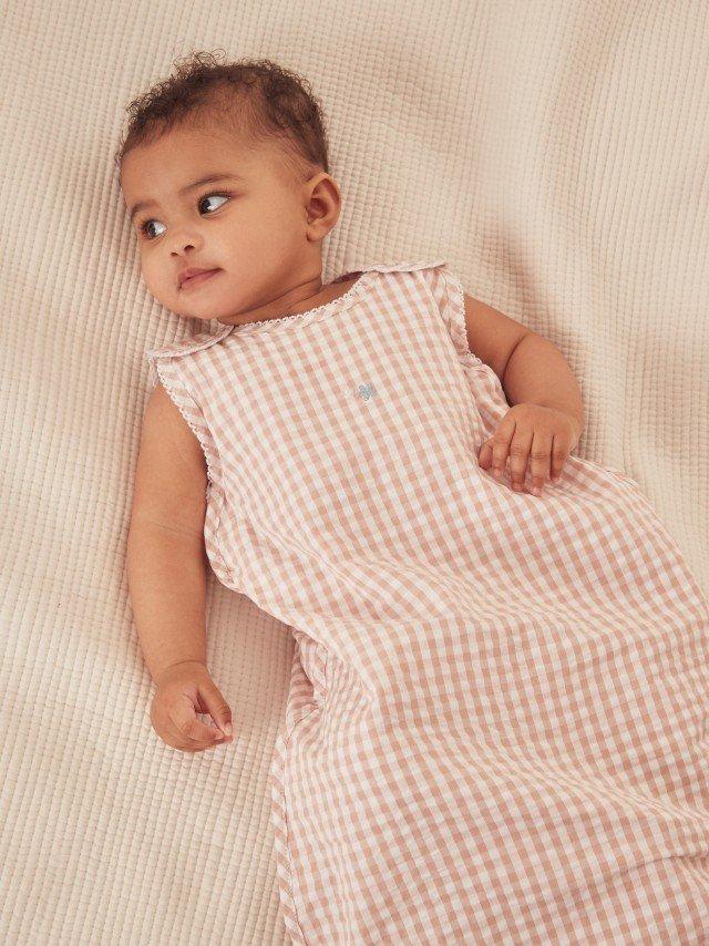 a baby laying on a bed wearing a pink and white checkered outfit
