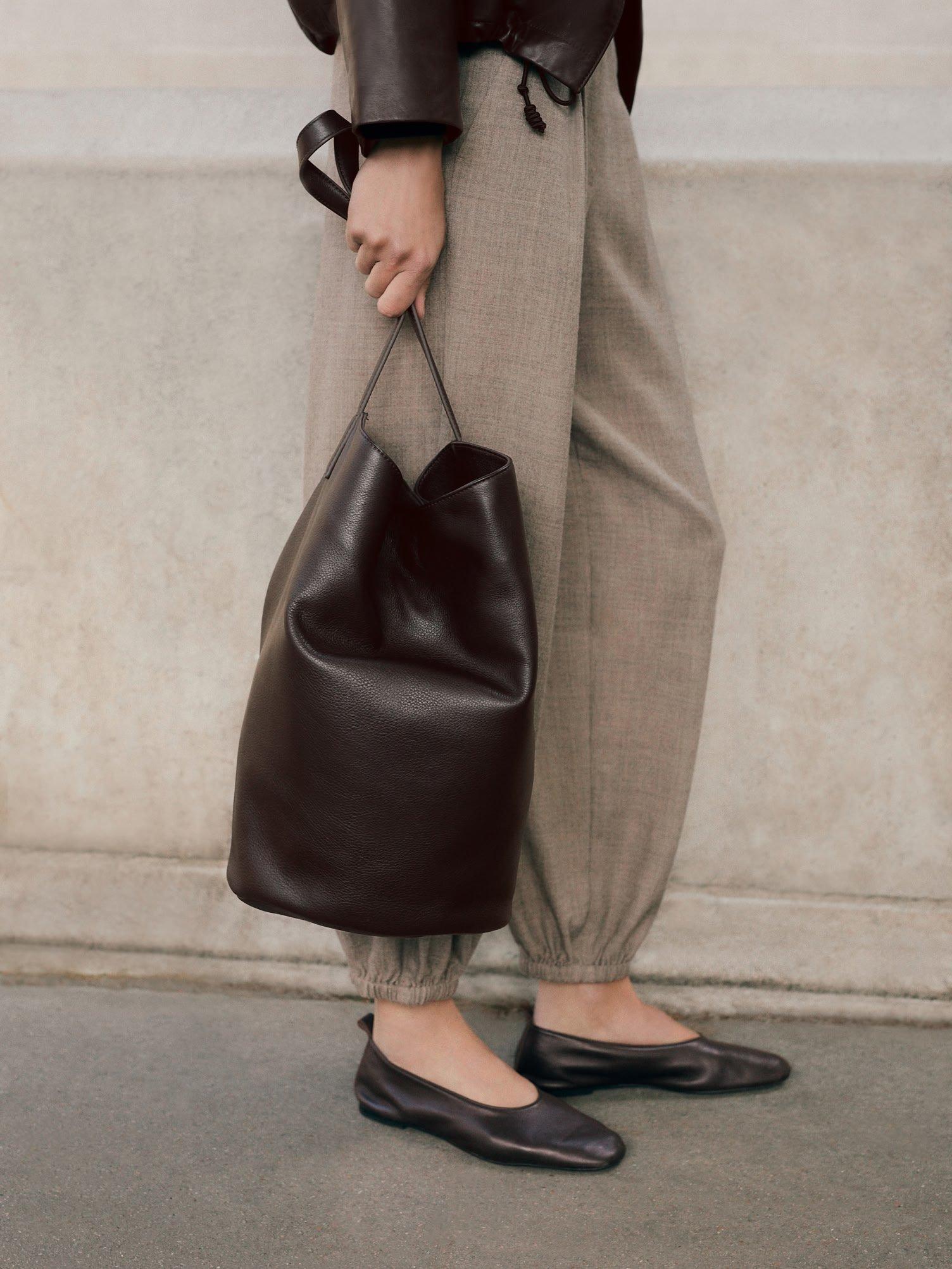a woman in a tan jacket and pants holding a brown bag