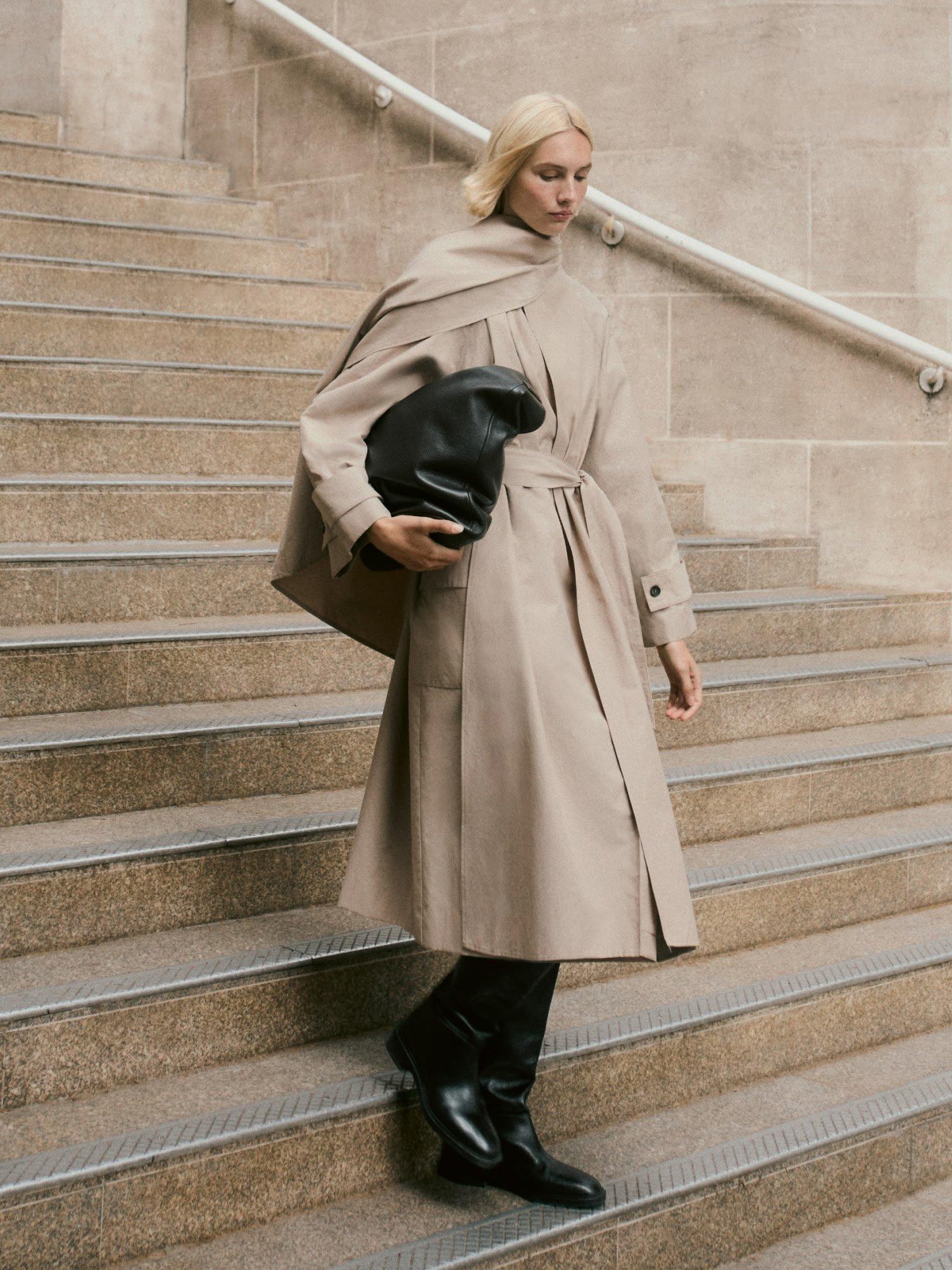 a woman in a trench coat and black boots on a set of stairs