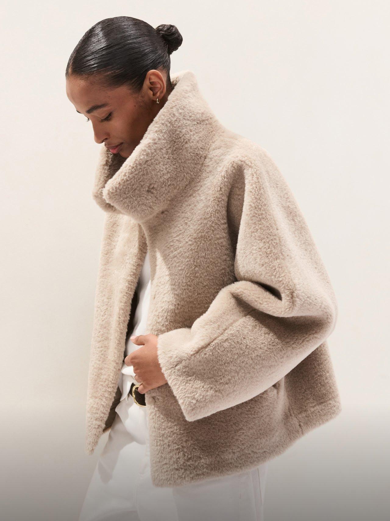 a woman in a beige jacket and white pants