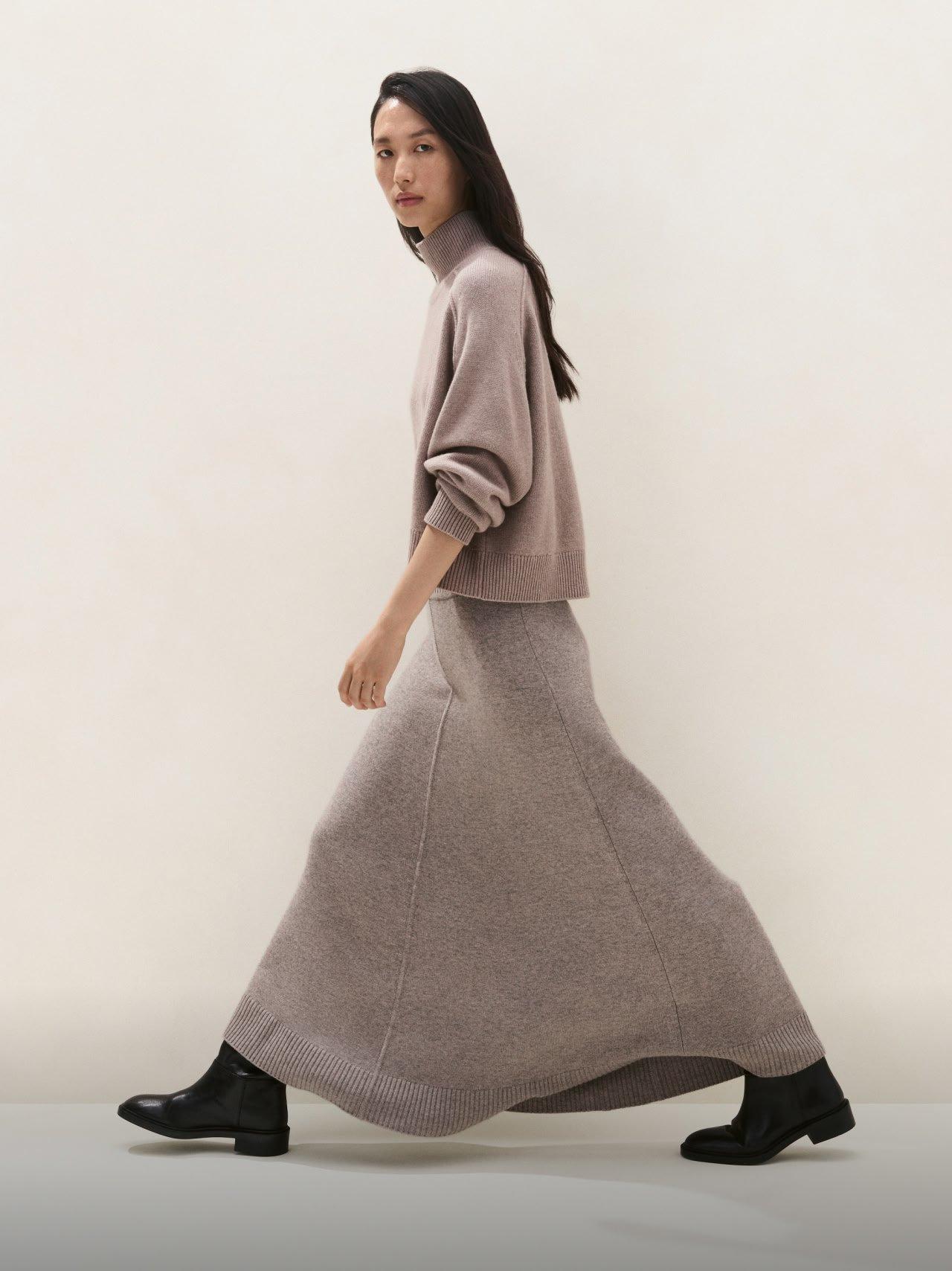 a woman in a long skirt and boots walking down a hallway