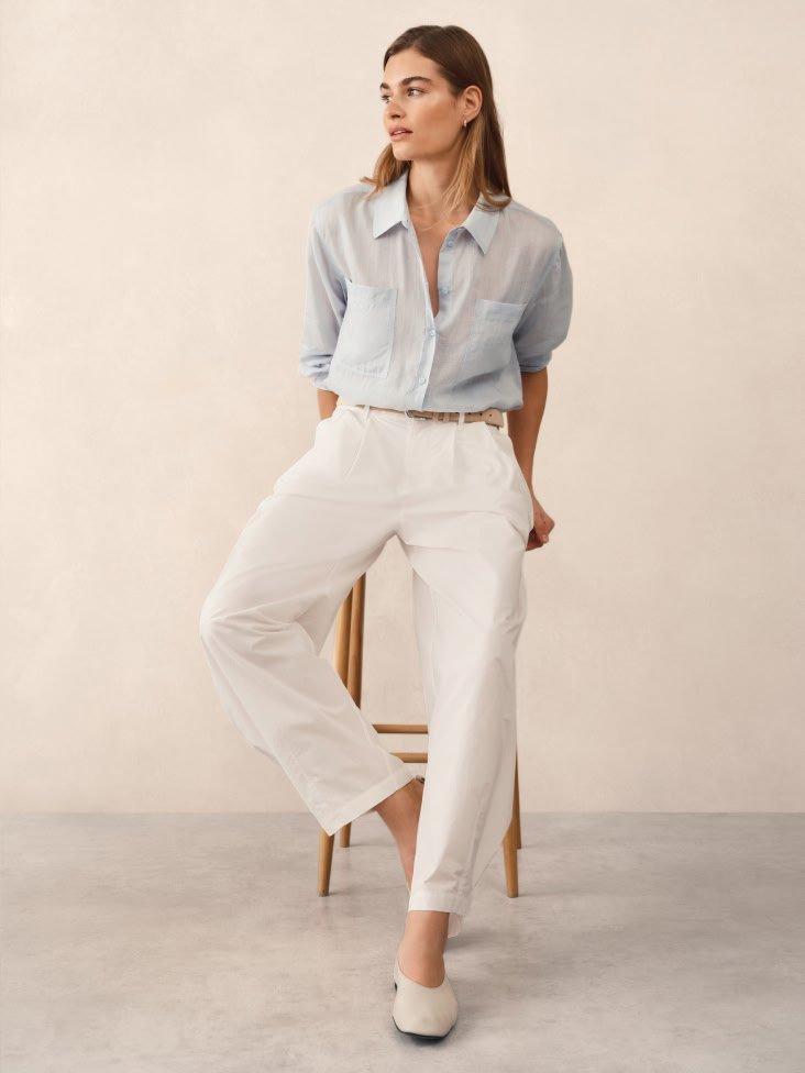 a woman sitting on a stool wearing white pants and a blue shirt