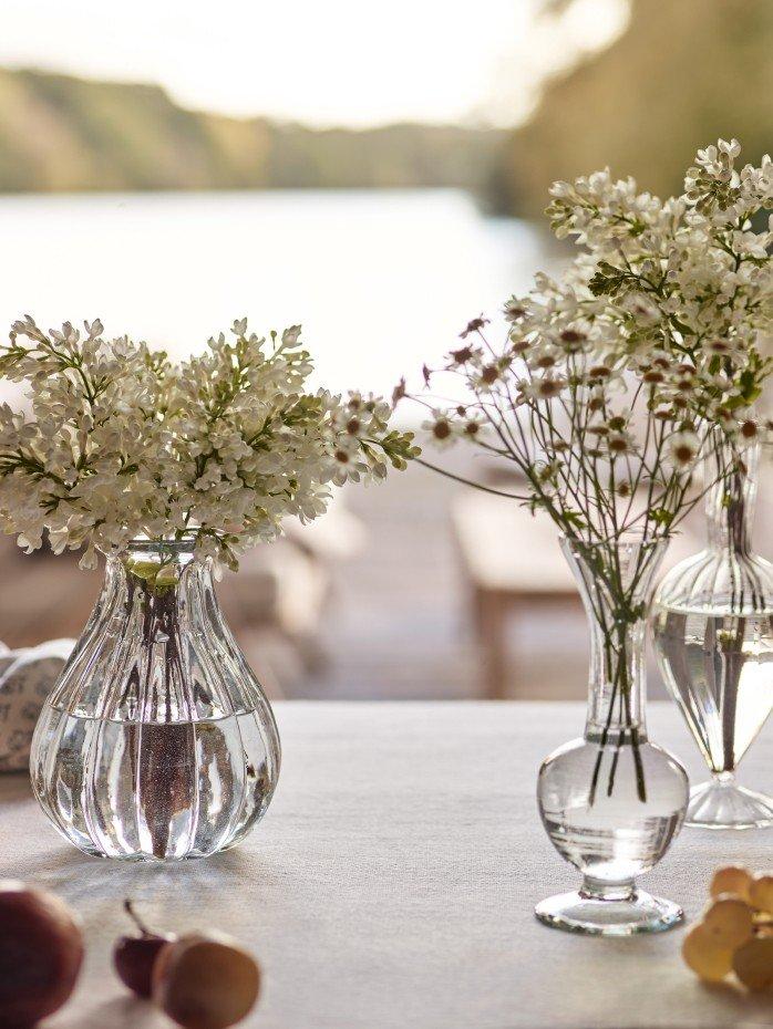 three vases of flowers on a table with a lake in the background