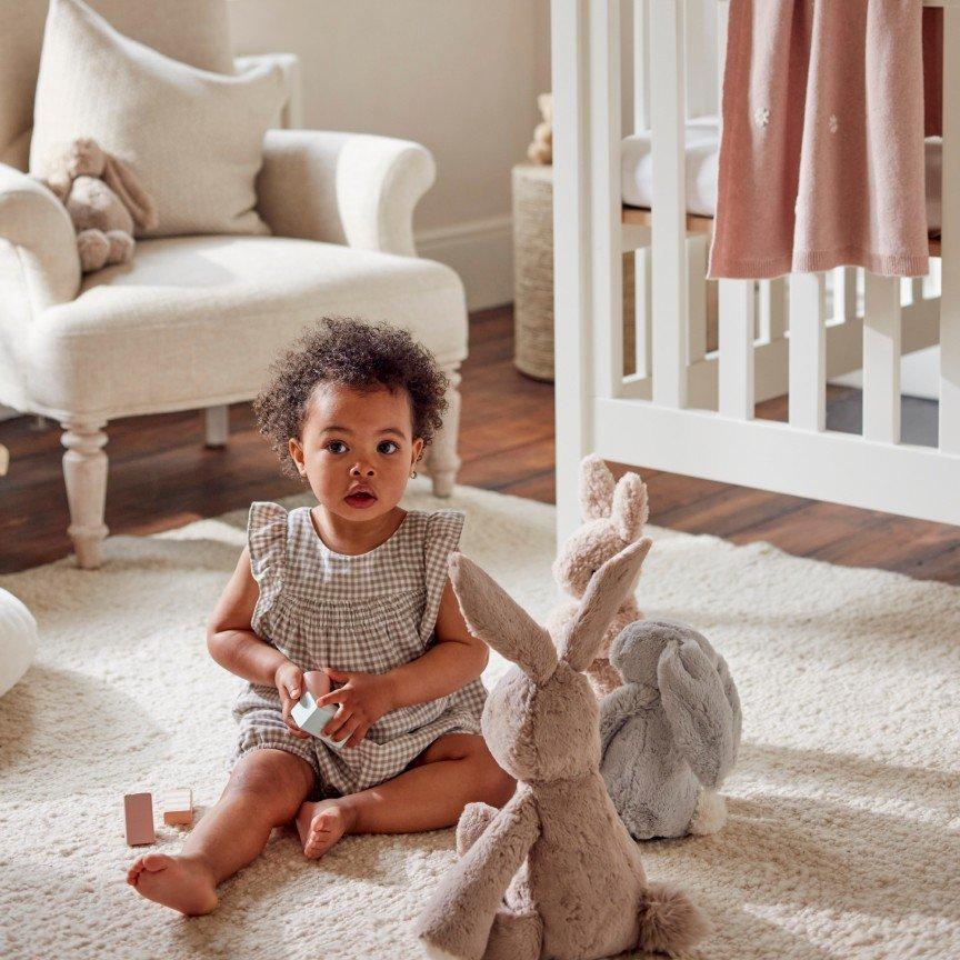 a baby girl sitting on a white rug in a nursery