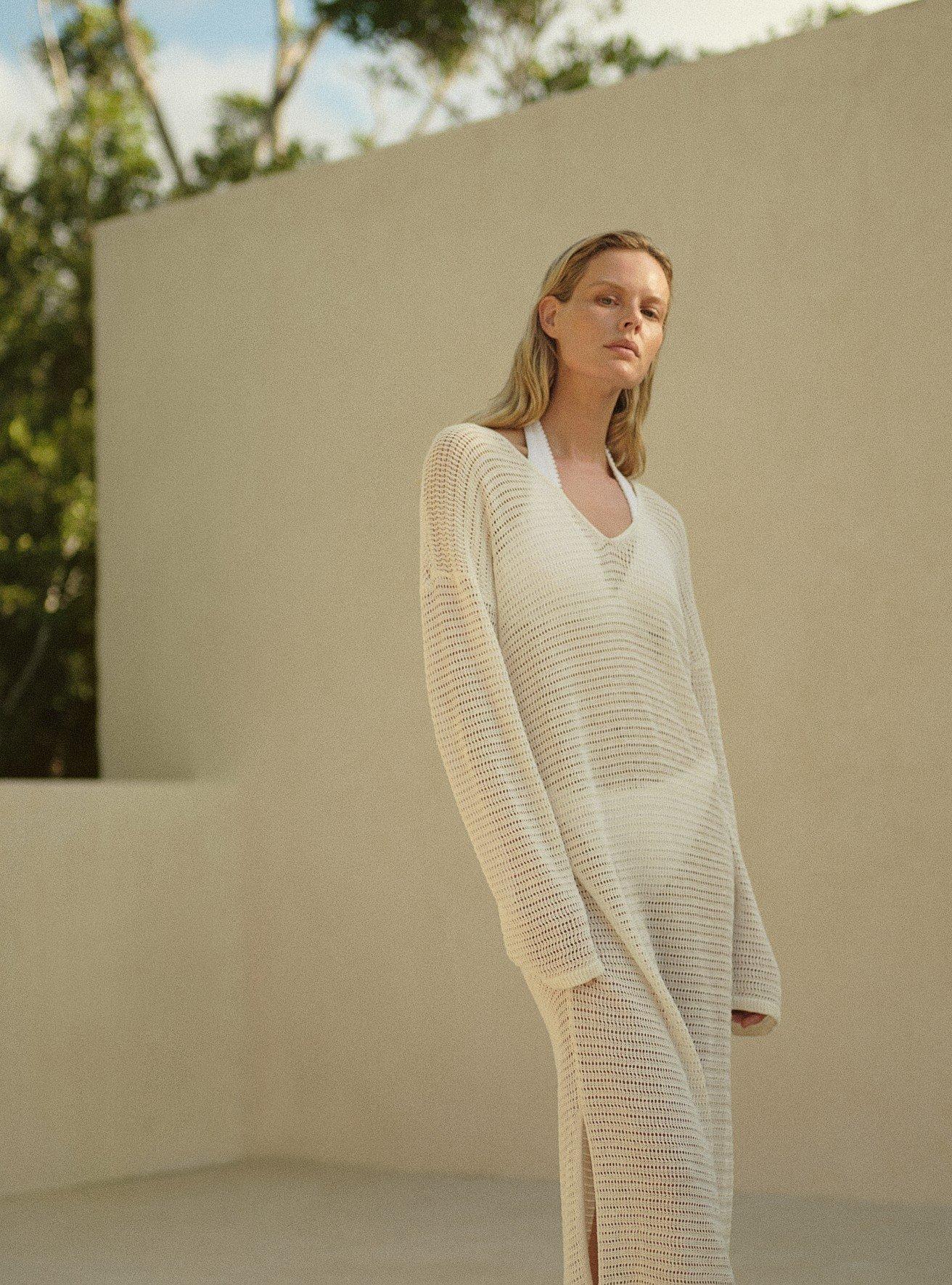 a woman in a long white sweater dress standing in a white room