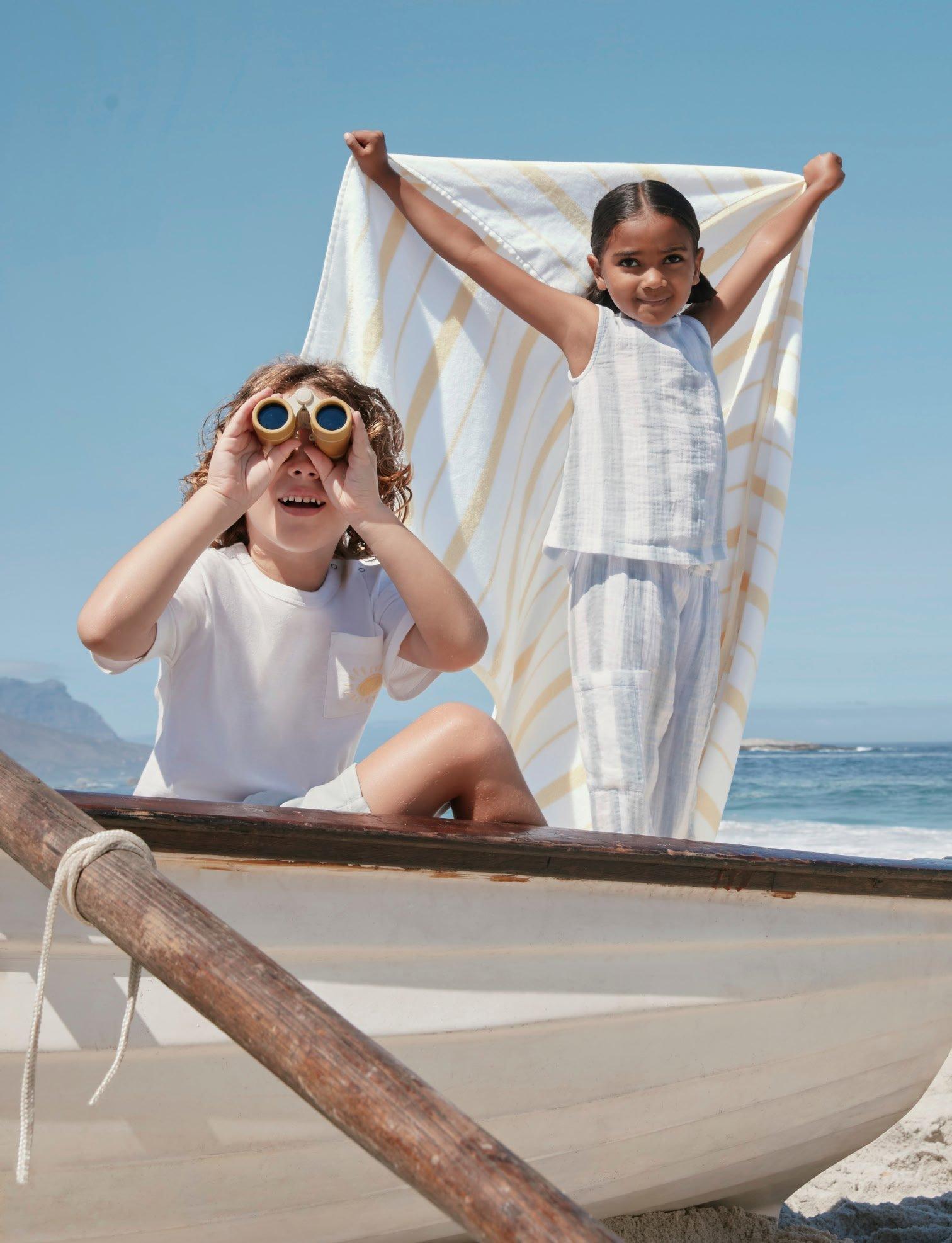 two children sitting in a boat on the beach with a towel