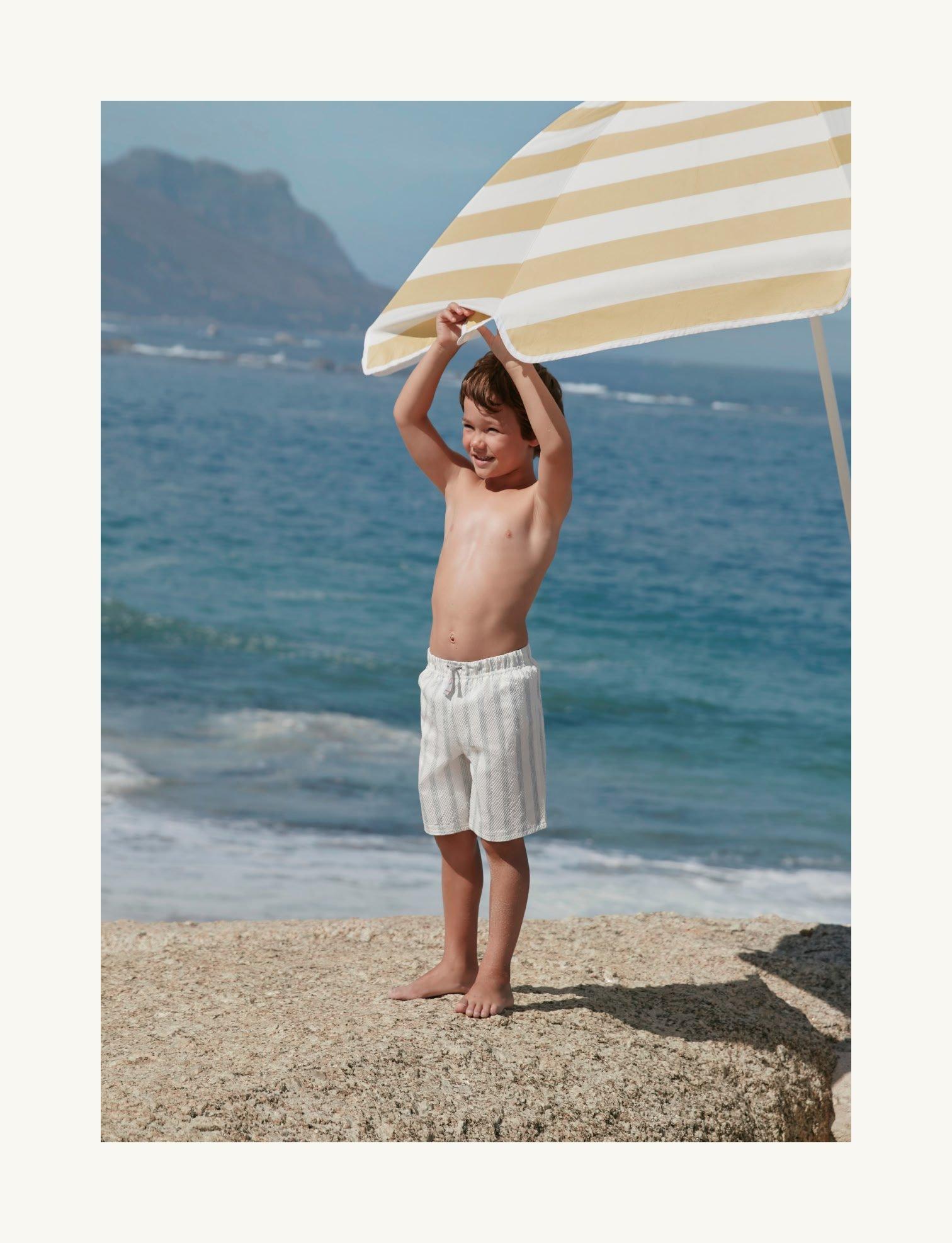 a young boy standing on a beach holding an umbrella