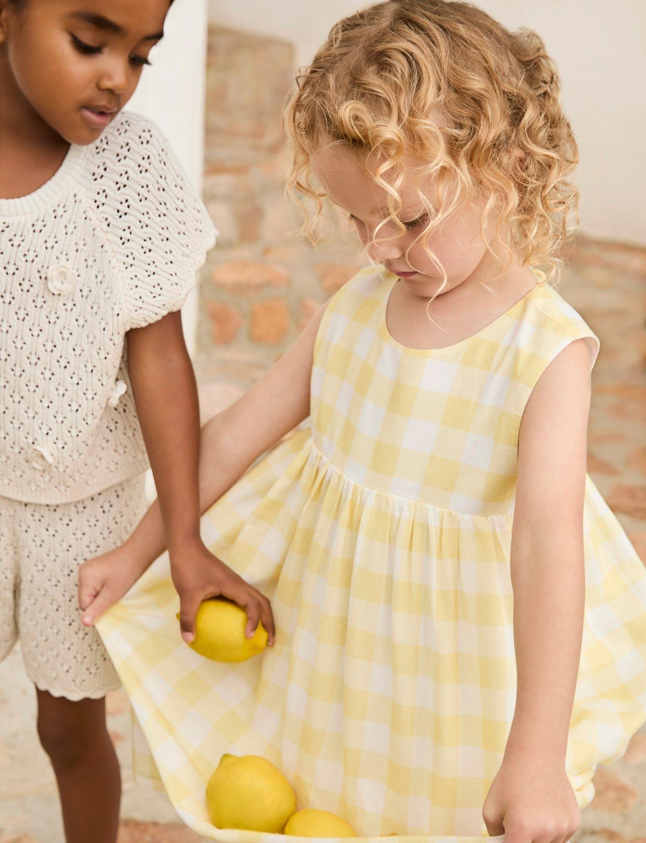 two little girls holding lemons in a basket with a yellow dress
