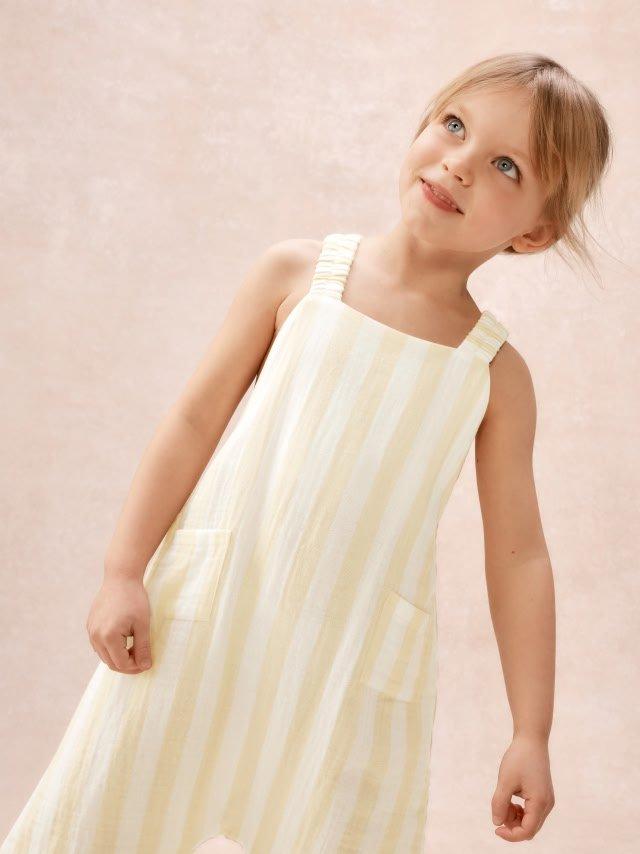 a little girl in a yellow dress standing up with her hands on her hips