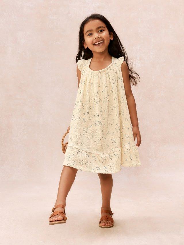 a little girl in a dress and sandals standing on a white floor