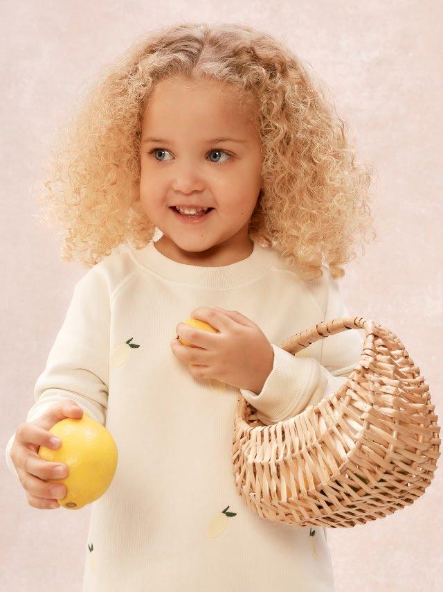 a little girl with curly hair holding a basket and a yellow ball