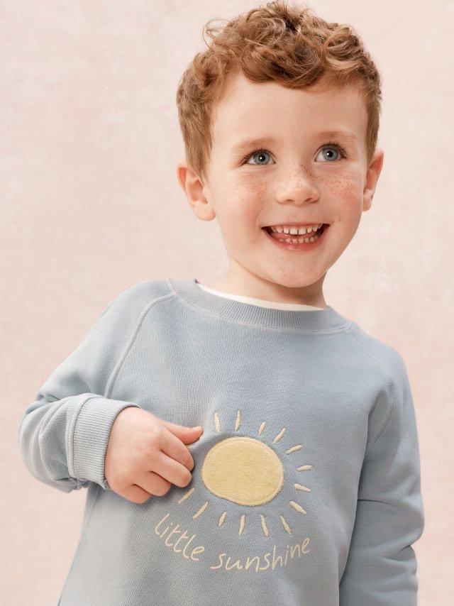 a little boy wearing a sweatshirt with a sun on it