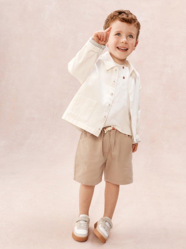 a little boy in a white shirt and shorts standing on a pink background